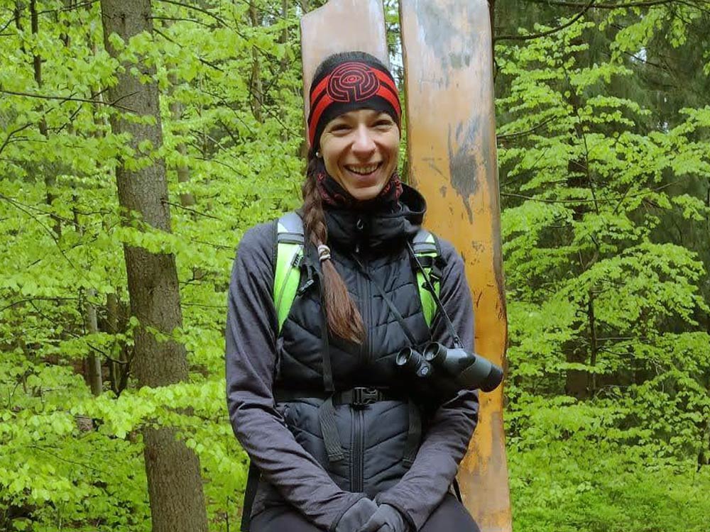 Woman sits on a wooden chair in the woods.