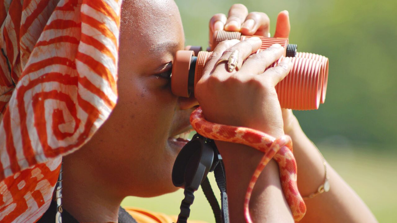 Woman with orange and white head scarf, orange binoculars and a patterned orange snake.